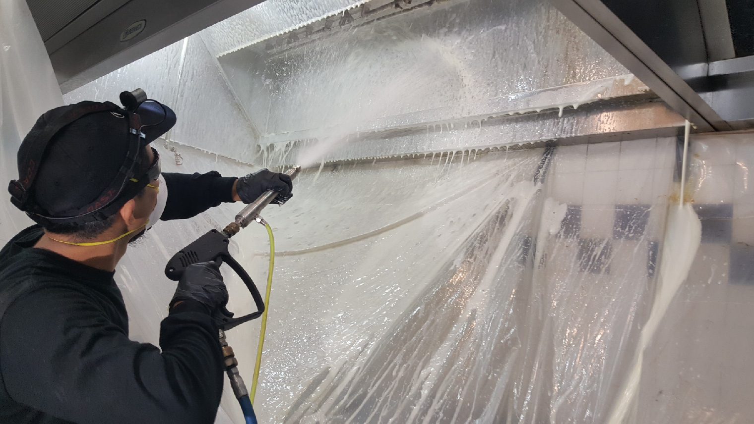 Hood cleaning 3 Person pressure washing a large plastic-covered surface indoors.