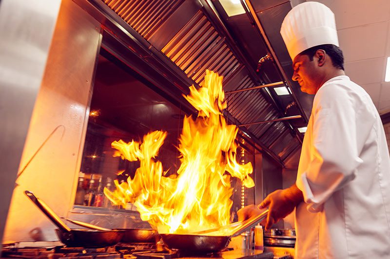 Chef cooking under hood 2 Chef cooking with dramatic flames in a professional kitchen.