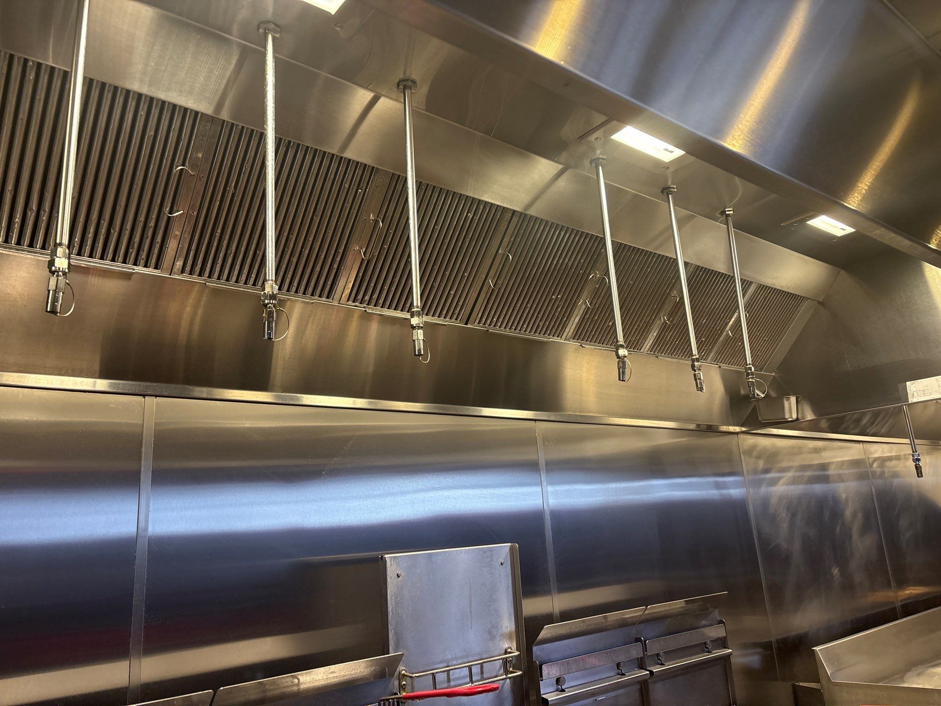 A commercial kitchen with stainless steel exhaust hoods and cooking equipment.