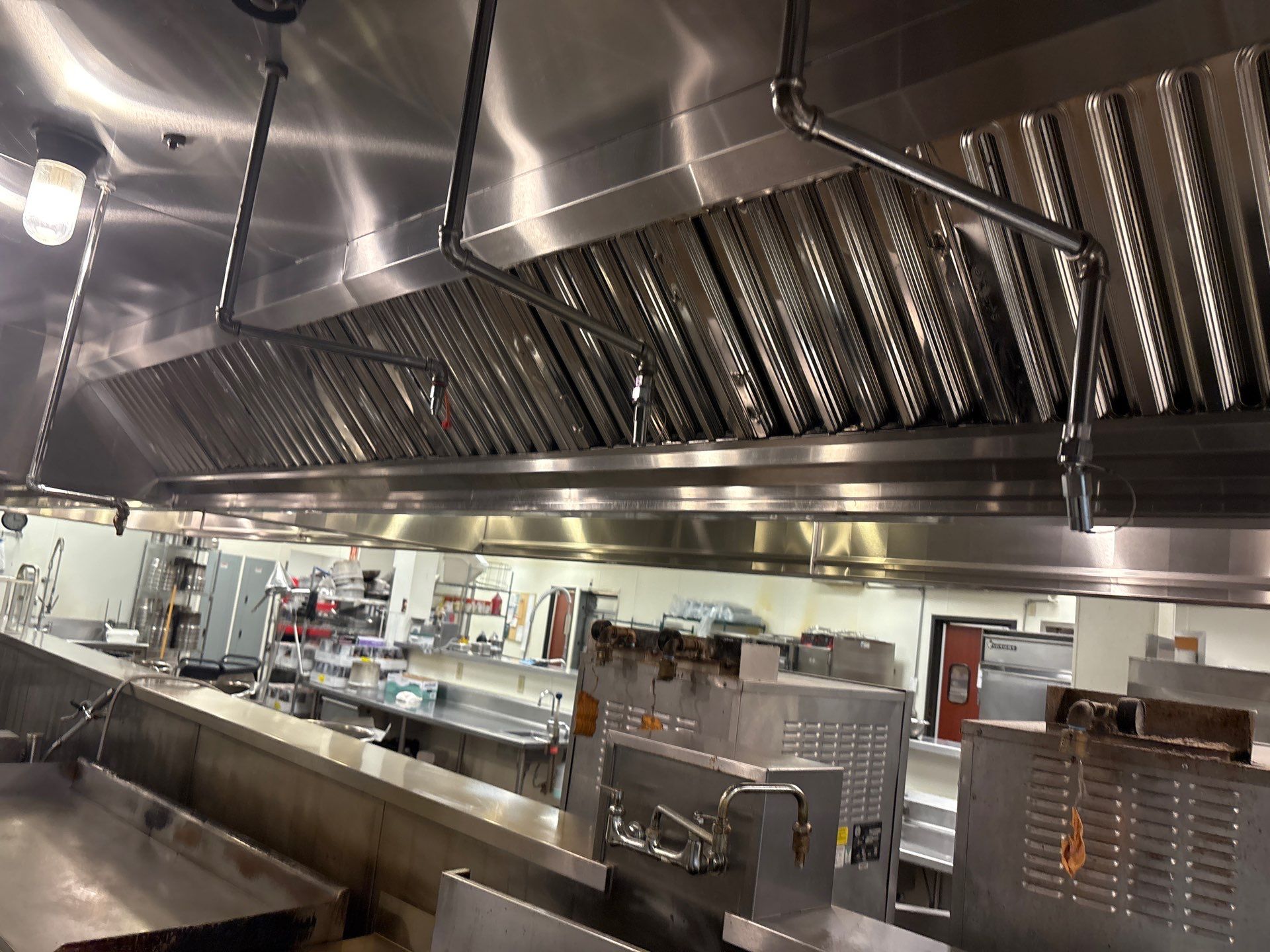 A clean, stainless steel commercial kitchen with cooking equipment and ventilation hoods.